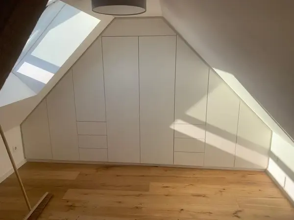 Einbauschrank im Dachgeschoss mit weißen Fronten und Dachfenster, modernes Design.