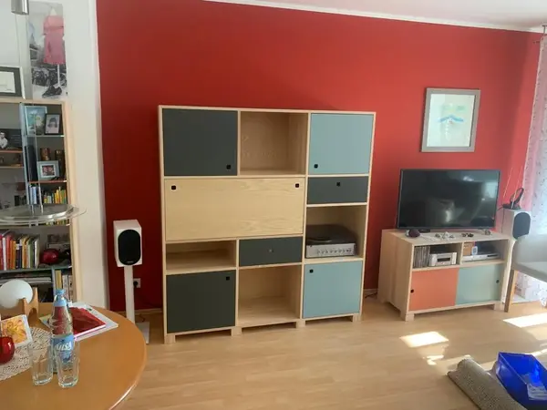 Modernes Wohnzimmer mit Holzmöbeln, Regalwand, Fernseher und roter Akzentwand.