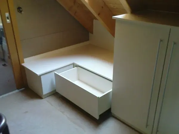 Weiße Einbauschränke mit Schublade unter Dachschräge als platzsparende Möbel-Lösung.