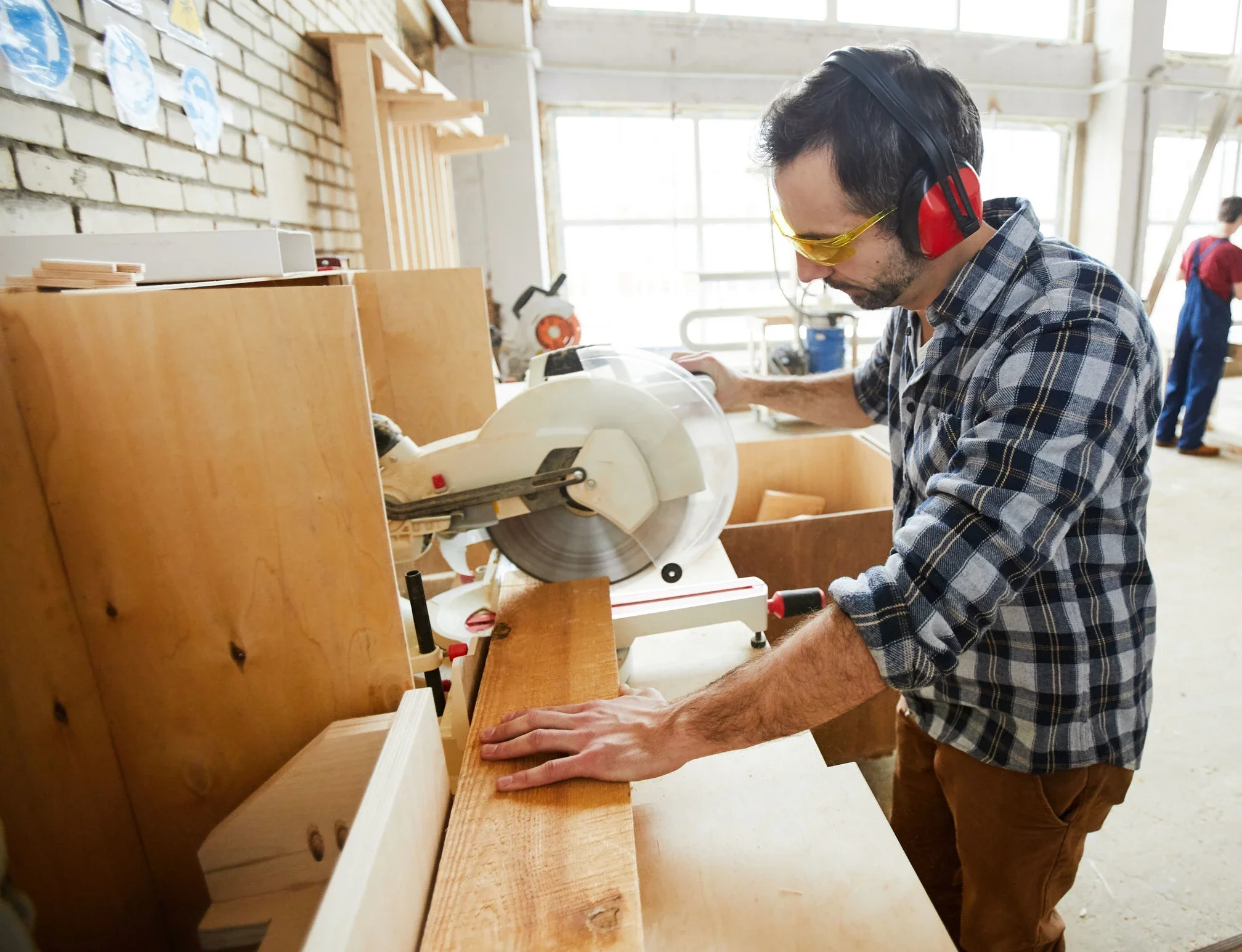 Ein Handwerker sägt Holz in einer modernen Schreinerei mit Gehörschutz und Schutzbrille.
